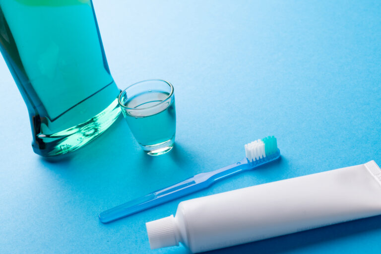 Image of cleaning liquid, toothbrush and toothpaste on blue surface. Health, dentistry, dental accessories and taking care of teeth concept.